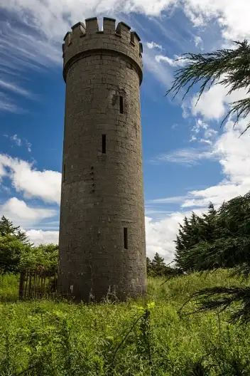 Round stone tower with crenellated top standing on the Hill of Allen beneath a blue sky.
